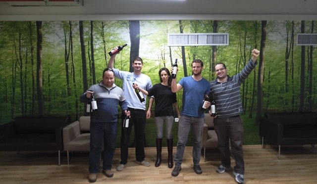 Five graduate students holding wine bottles and smiling